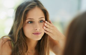 Young woman looking at her skin around eyes in the mirror.