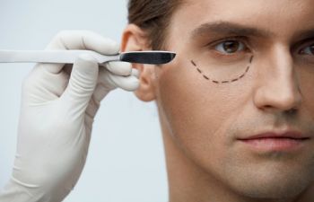 A plastic surgeon drawing marks around eyes of a handsome man
