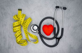 a pillow in a shape of red heart surrounded by a stethoscope and a measuring tape